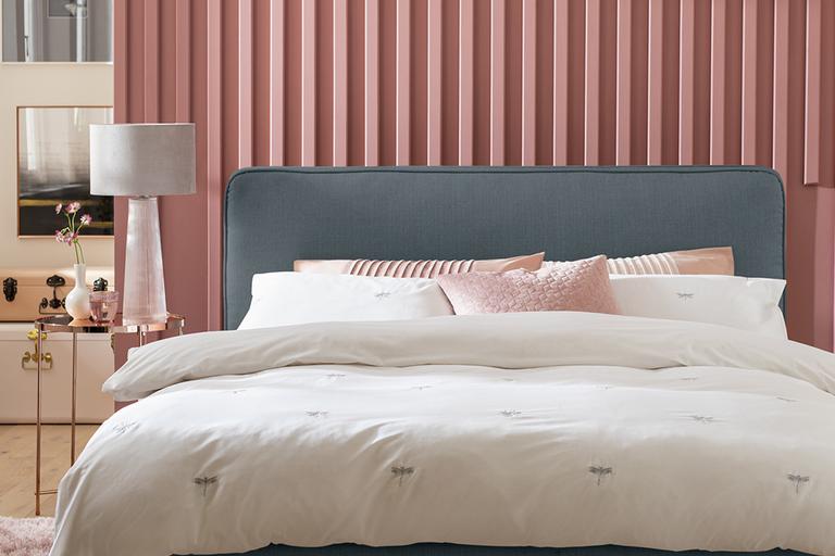 A grey ottoman bed with pink and white bedding on it.