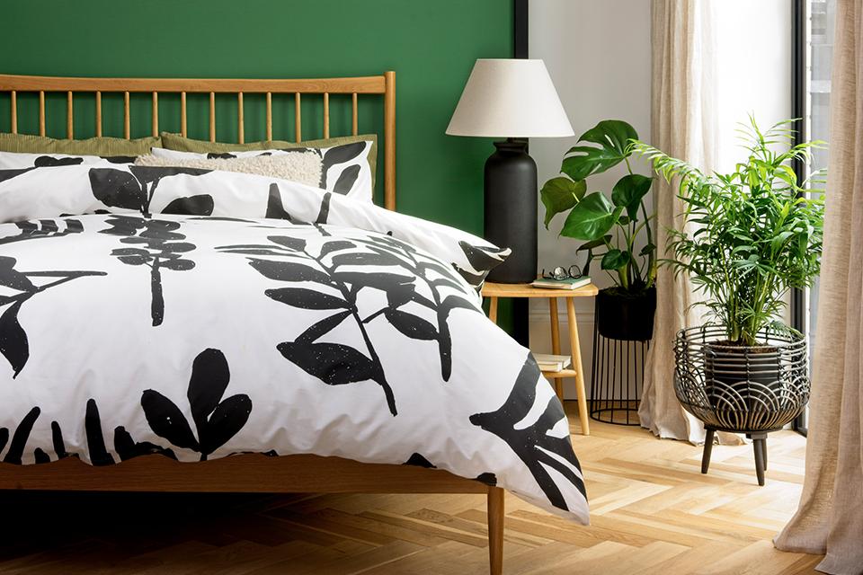 A nature-inspired bedroom with black and white leaf printed bedlinen on the bed.
