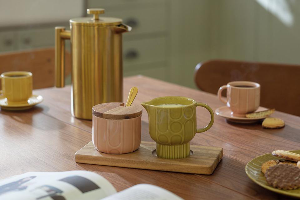 Pink and green mugs on a wooden dining table.