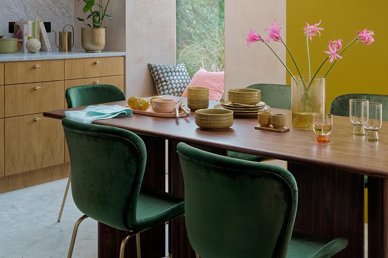 Small wooden dining table with green velvet chairs.