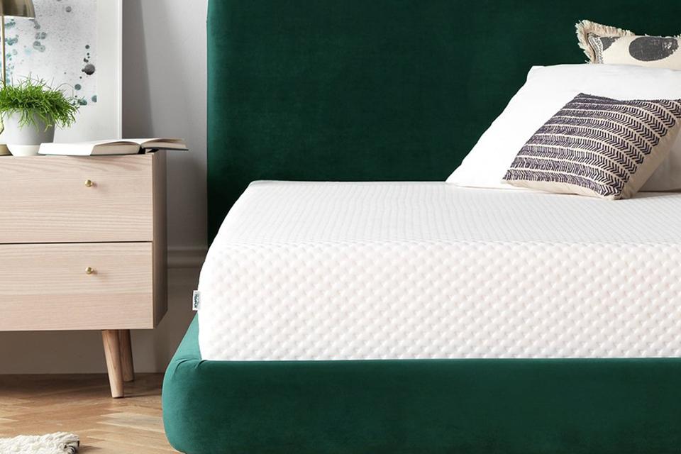 A green bed with white mattress and cushions.