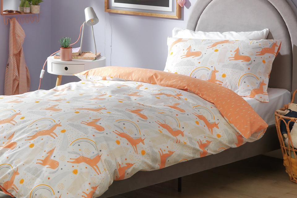 A kids bed with orange unicorn print bedding on a grey bed.