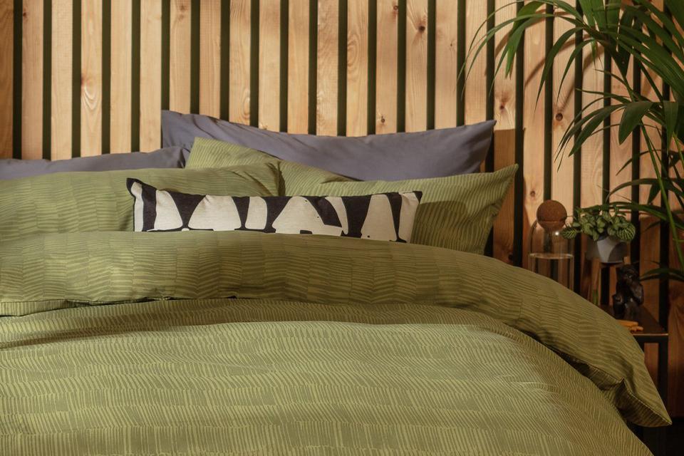 A bed in front of wooden panels with olive green bedding.