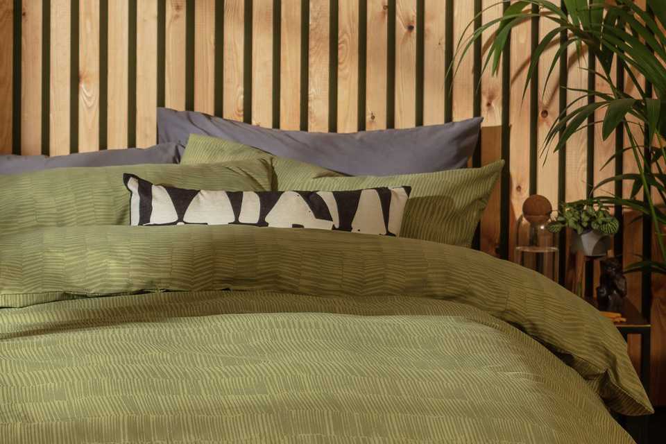 Green linen bedding on bed with wooden headboard.