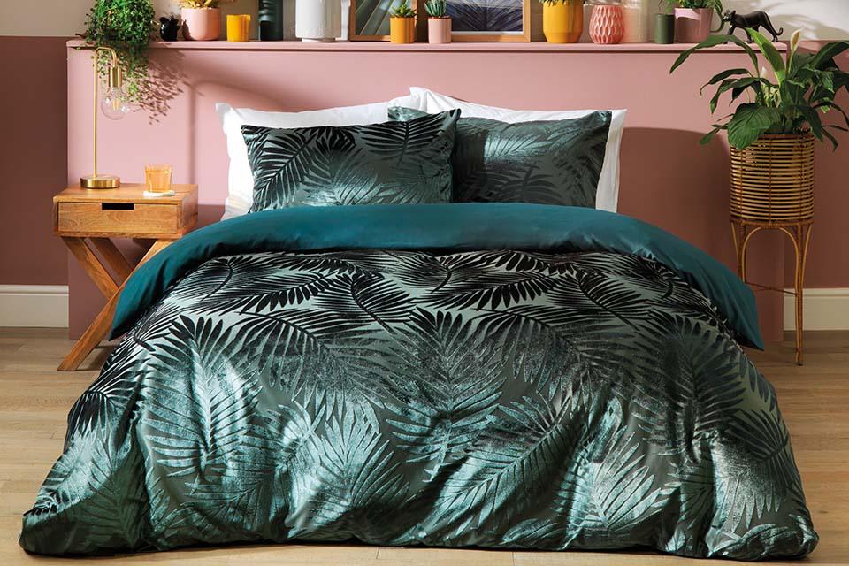 A green, velvetty leaf printed bedding on a bed.