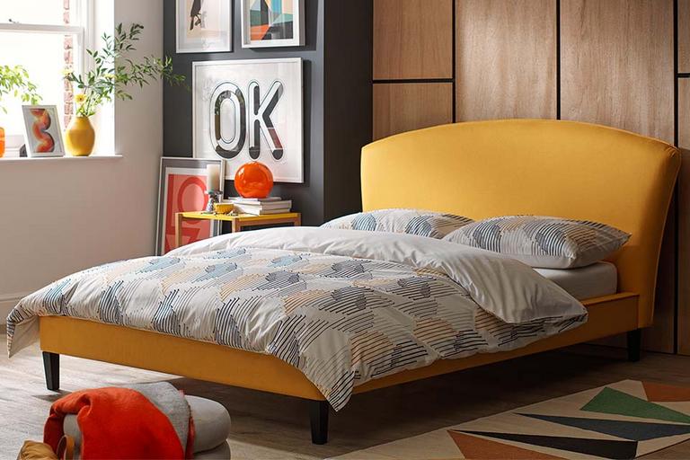 A modern bedroom interior with a mustard bed and abstract-theme bedding.