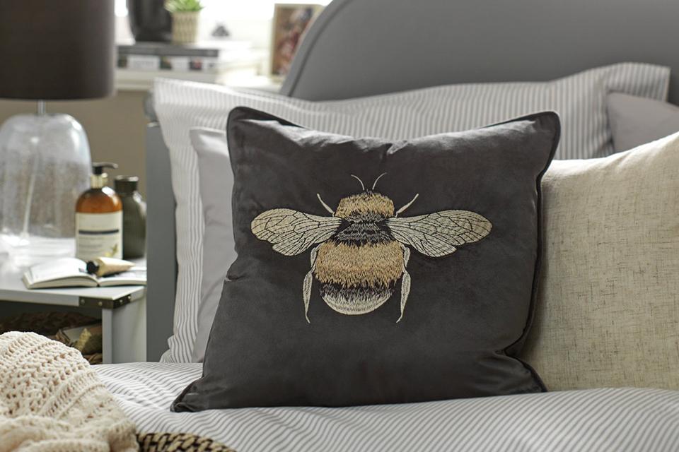 A bee embroidered grey cushion on a sofa.