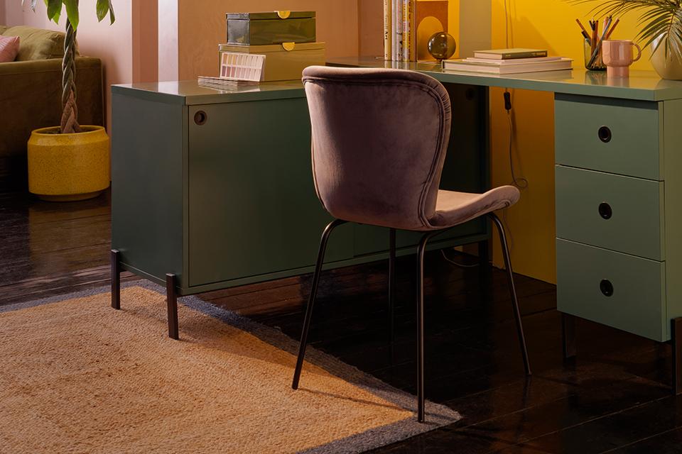 A green office desk with storage and a pink velvet chair.