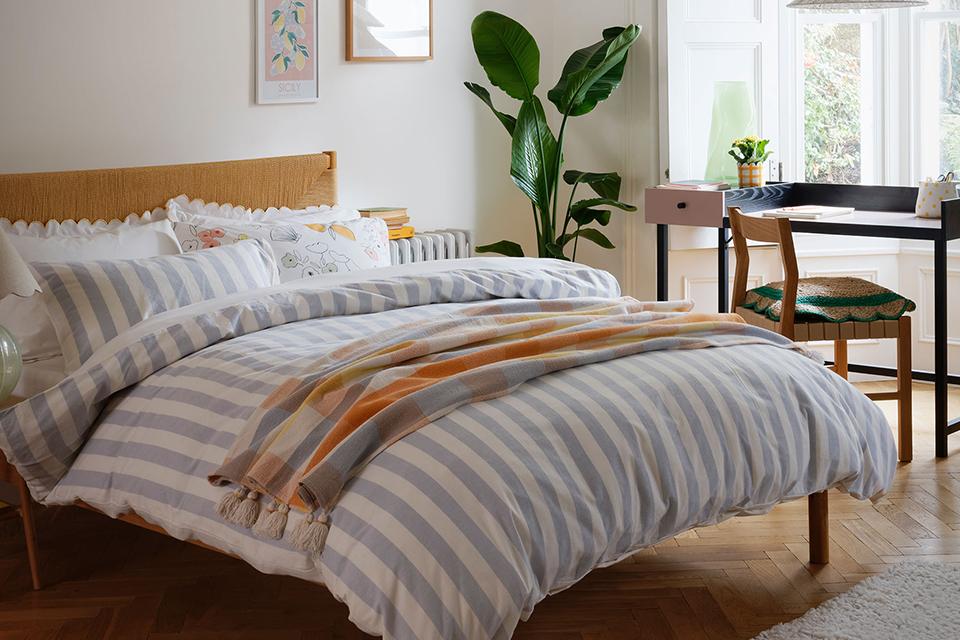 A wooden bed with blue and white stripe print bedding, scallop-edged pillows and a throw on it.
