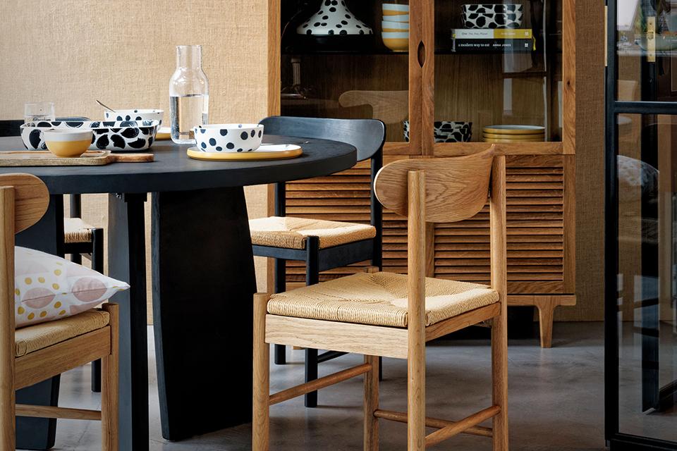 A dining room with black dining table, black and wooden finish chairs, cabinet and monochrome tableware.
