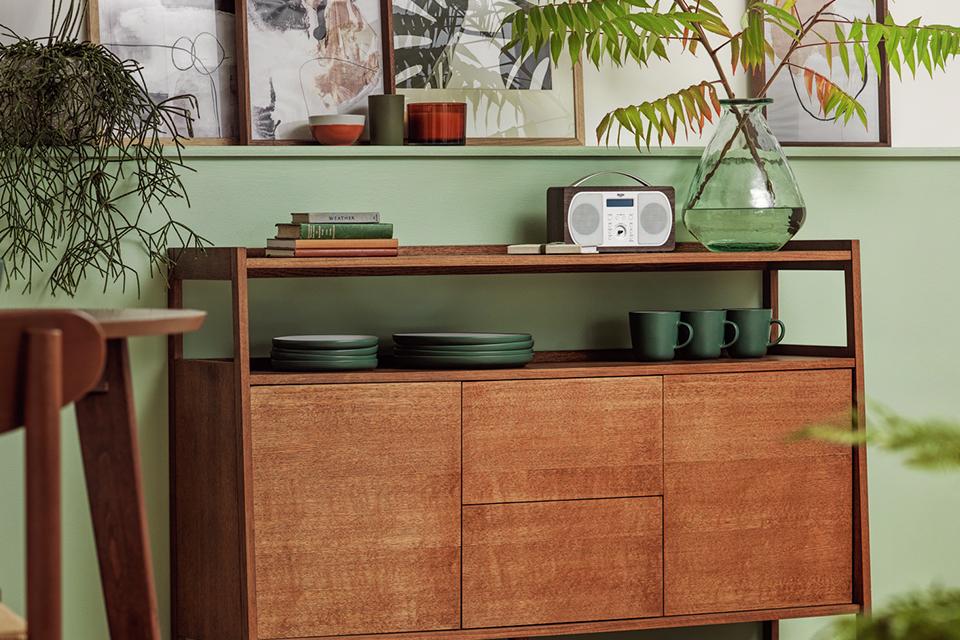 A natural finish storage cabinet in a dining room with dark green tableware on it.