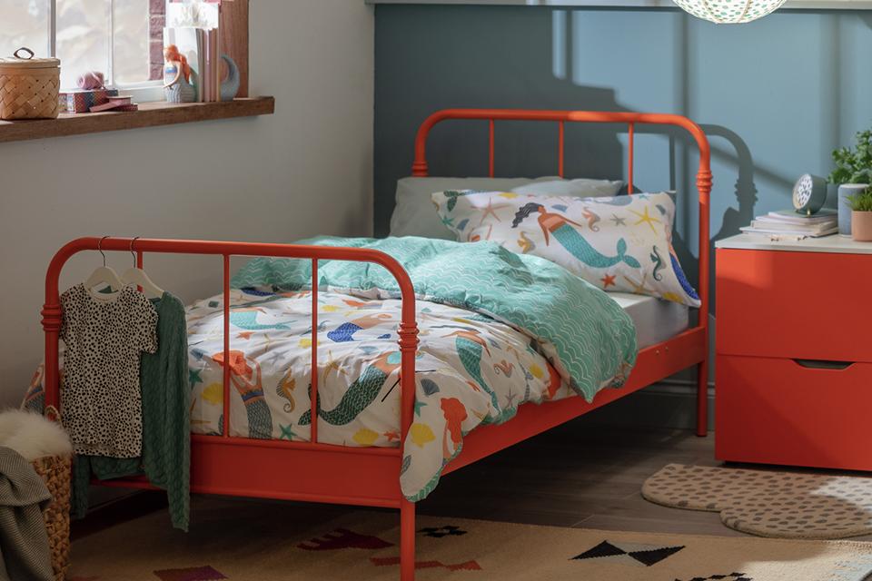 A metal kid's bed and orange bedside table in a grey and white kid's bedroom.