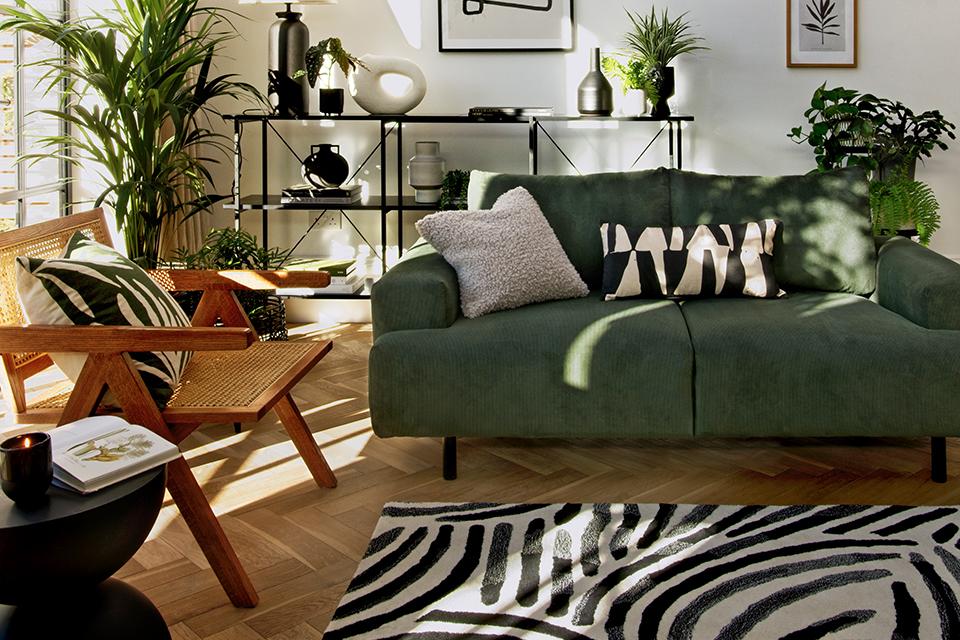 A living room with a green sofa, monochrome rug, cushions, wooden chair and houseplants. 