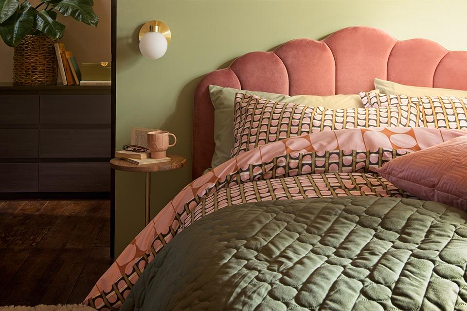 A pink velvet bed in a green bedroom with brass accessories.