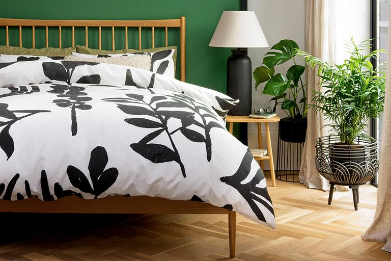 A wooden bed with leaf print bedding in monochrome.