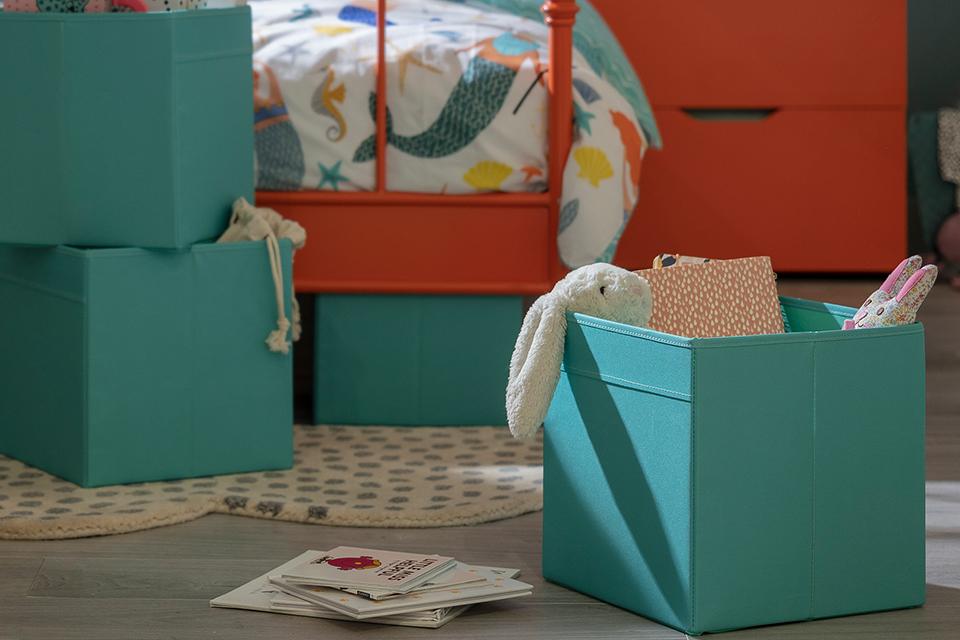 A set of canvas storage boxes in teal green placed on the floor in a kids's bedroom.