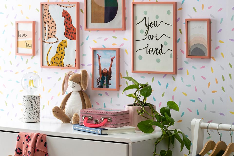 A set of wall art frames displayed in a multi-coloured kid's room with a white chest of drawers and other home accessories.