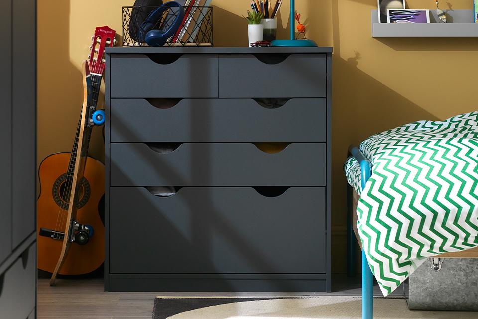 A kid's bedroom with dark grey storage and a guitar next to it.