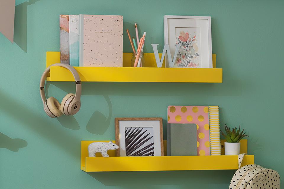A set of stationary including pencils and notebooks displayed on a yellow shelf in a green bedroom.
