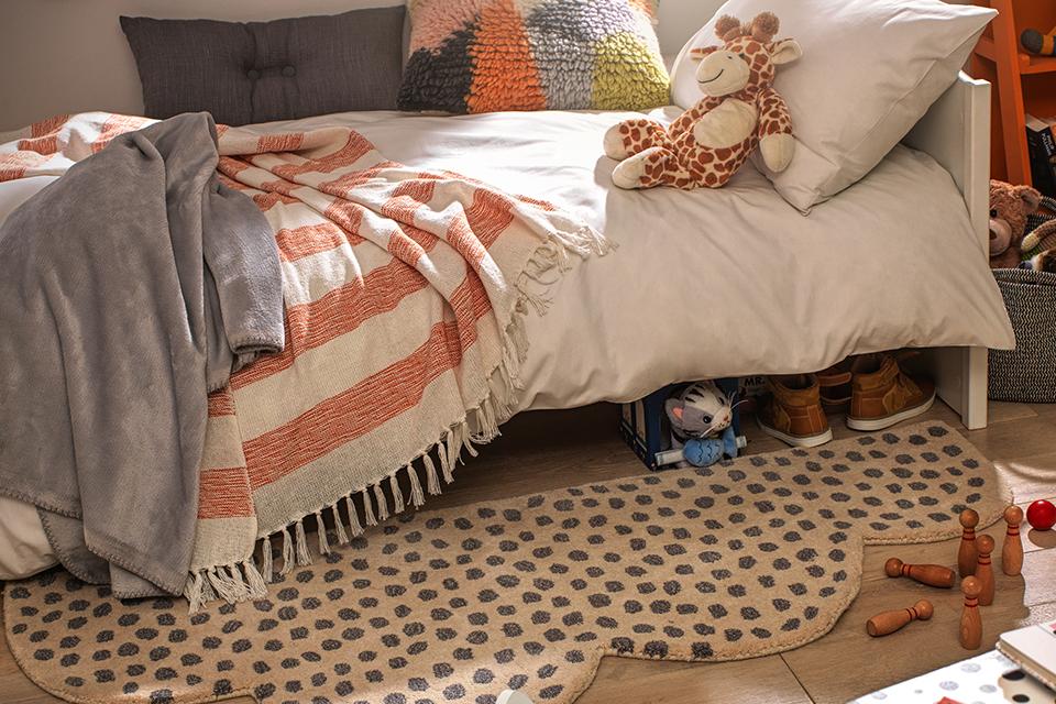 A kid's bed with white bedding and an animal print rug on the floor.