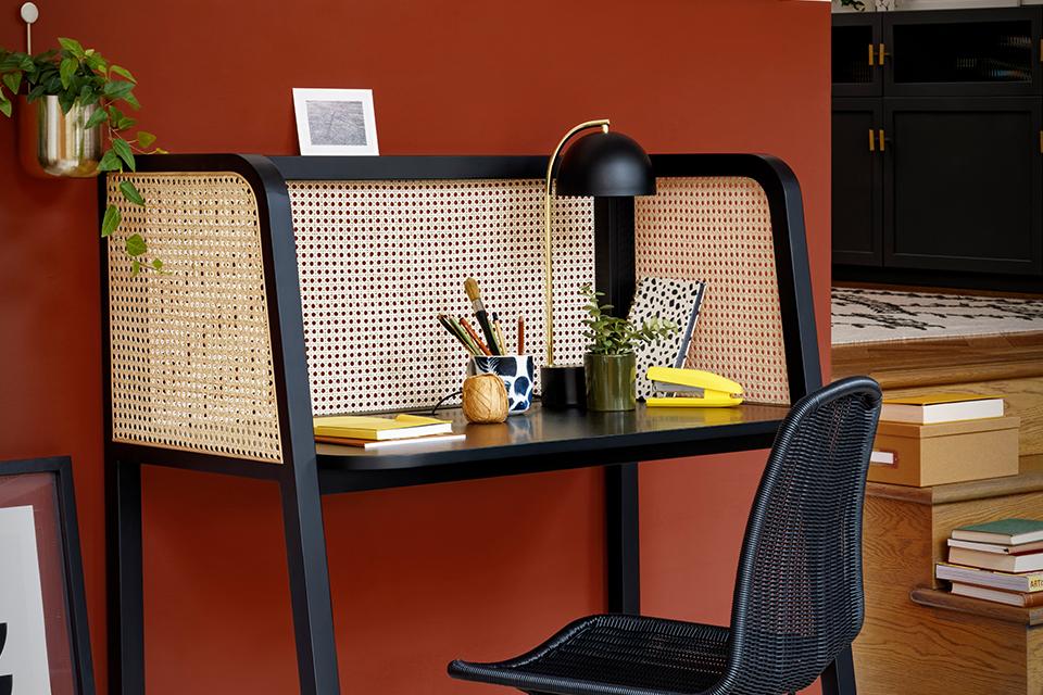A cane work desk with a black metal chair in rattan effect. 
