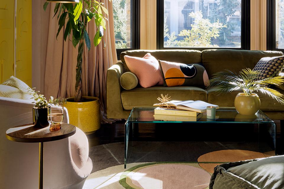 A yellow living room with green sofa, indoor plants, glass coffee table and green floor lamp.