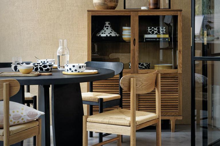 A dining room with rattan lamp, black table and wooden chairs.