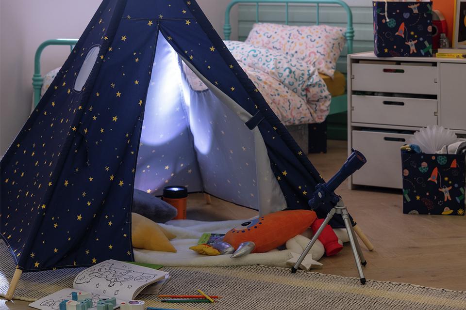 A blue space print kid's tent and storage boxes in a bedroom.