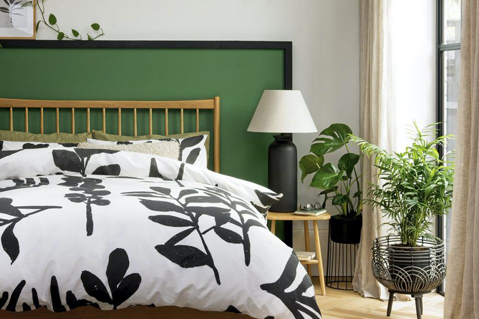 A green and white bedroom with a wooden bed featuring large leaf print bedding.
