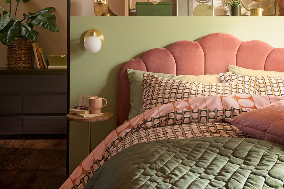 A pink velvet bed in a green bedroom with brass accessories.