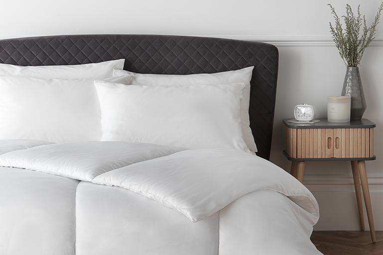 A dark grey bed with white Habitat supersoft washable 15 tog duvet and pillows on it. 
