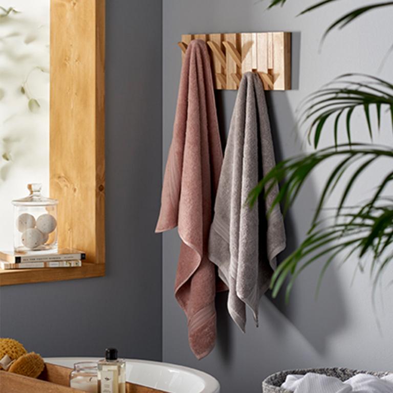 A natural finish overdoor hanging storage with grey and pink hand towels on it.