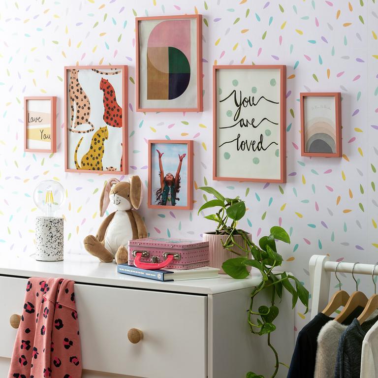 Four wall art frames hanging on a confetti wall.