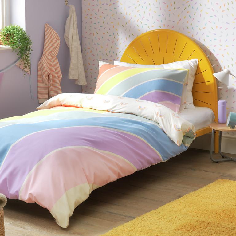 A light rainbow coloured bedding on a single bed.