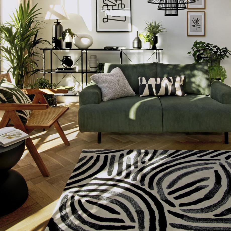 A nature-themed living room with black and white rug and an olive-green sofa.