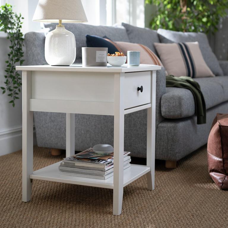 A white, one-drawer side table beside a sofa in a living room.