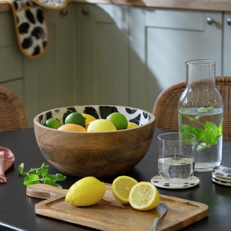 A wooden mixing bowl containing limes and lemons on a kitchen table.