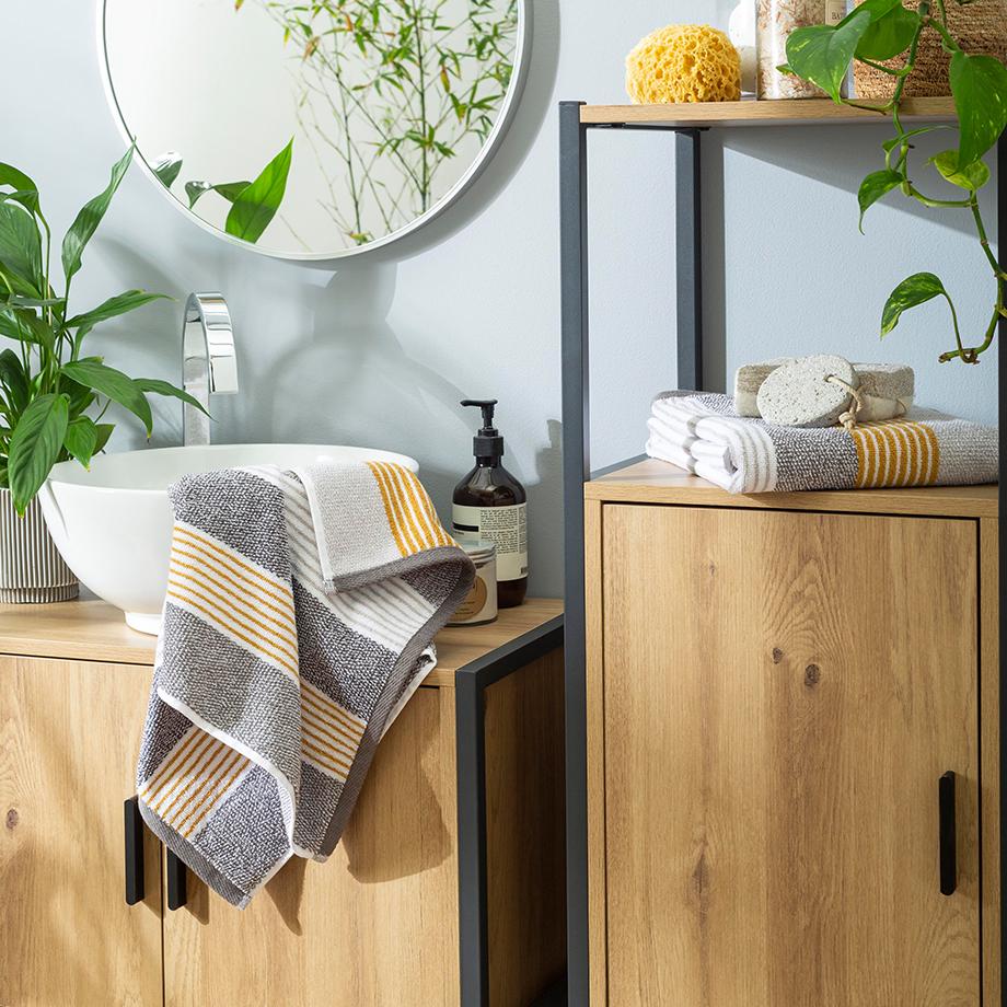 A bathroom with wooden and black framed furniture, white sink and striped hand towels in grey, white and yellow. 