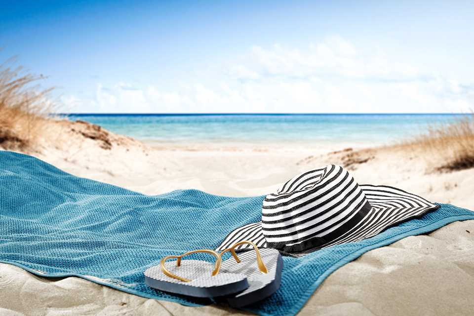 Blue towel under a hat and shoes on a beach.