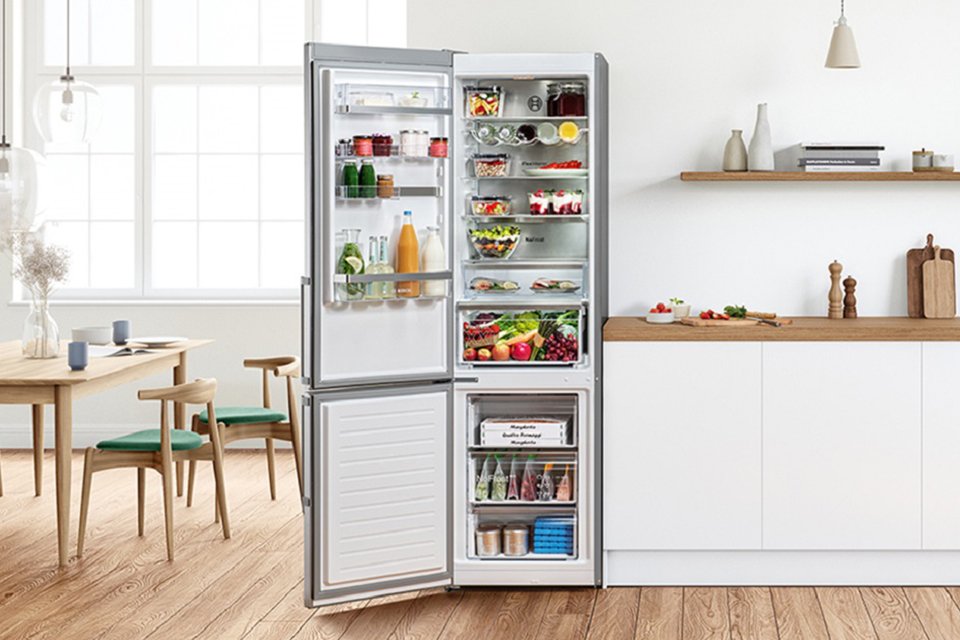 A Bosch silver freestanding fridge freezer stocked with food and drinks in a dining room setup.