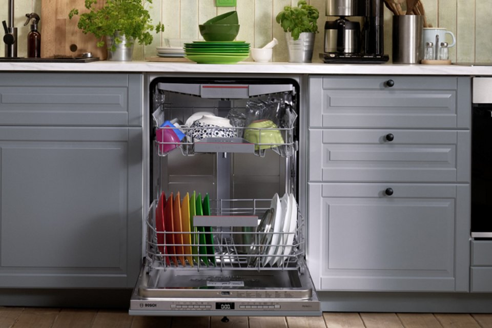 A Bosch silver integrated dishwasher with crockery inside it in a kitchen setup.