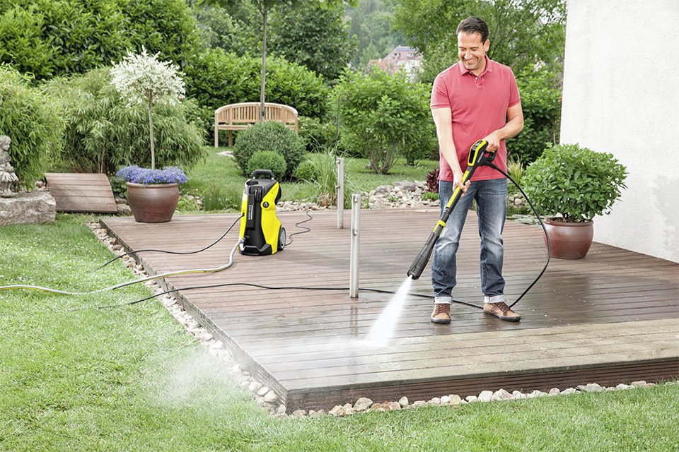 A man using a Karcher pressure washer to clean a patio deck.