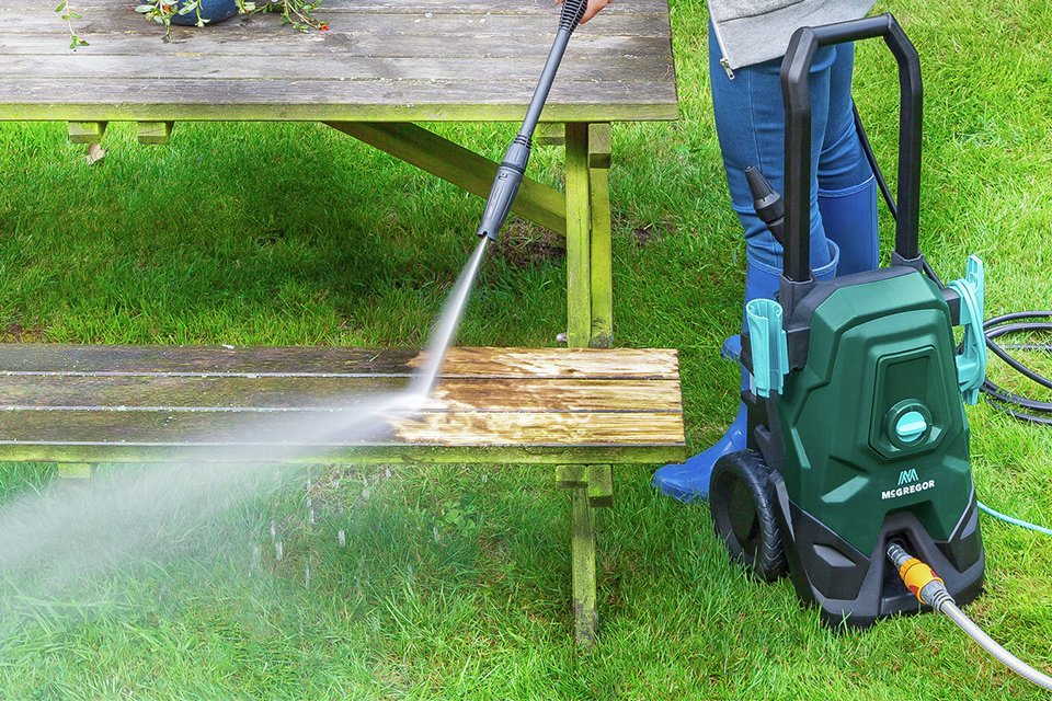 Gardener using a McGregor pressure washer to jet away dirt from a bench.