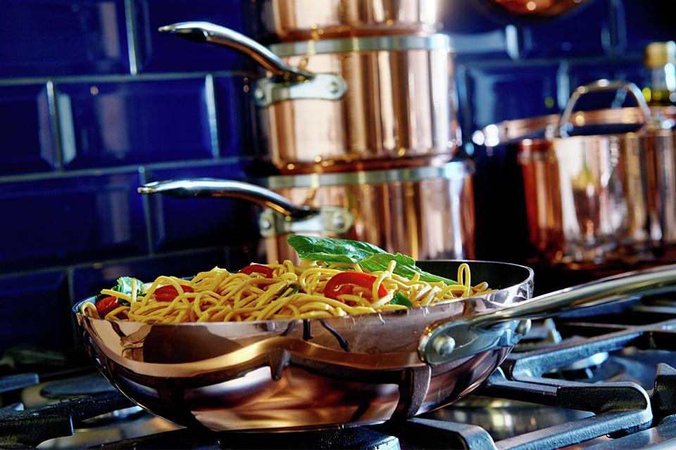 Image of a copper wok on a hob in a blue tiled kitchen.
