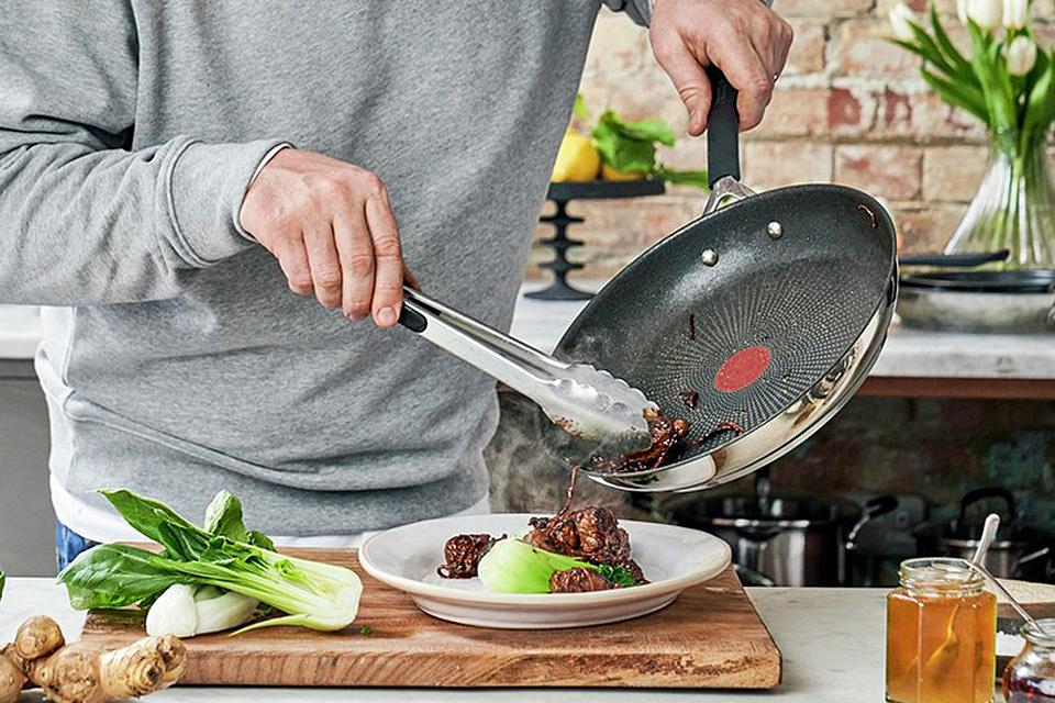 Image of someone serving meat and vegetables onto a plate from a saute pan.