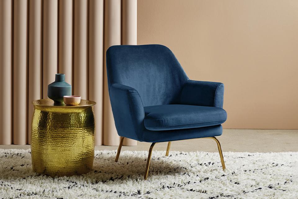 Image of a navy, velvet cocktail chair next to a gold metal side table.