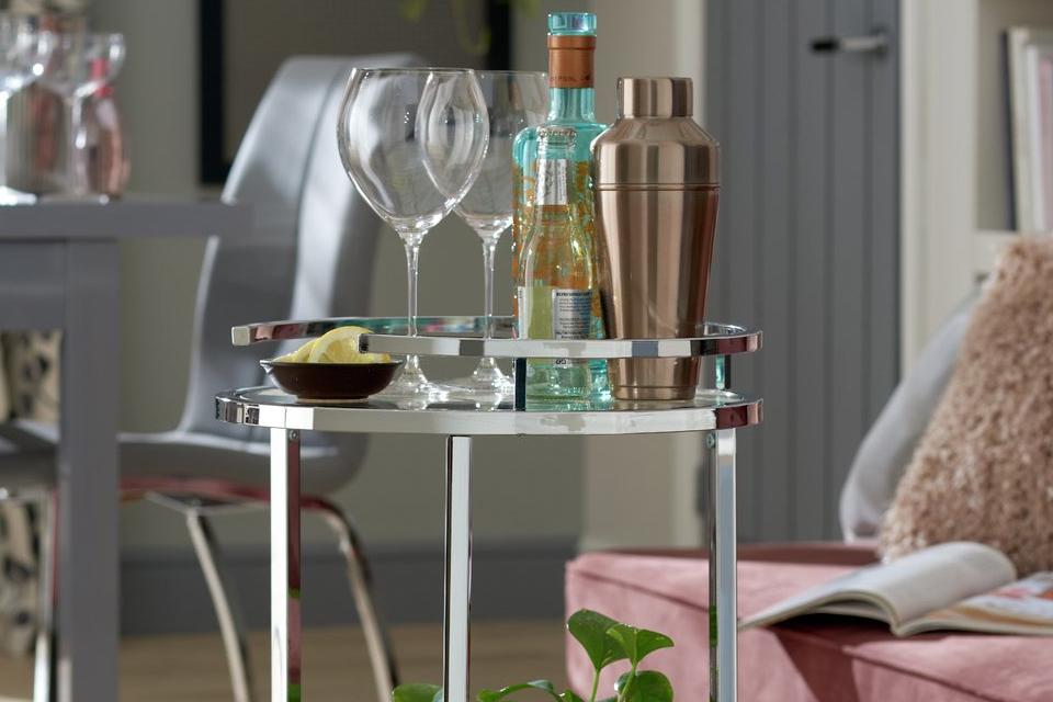 Image of a round, chrome drinks trolley with glasses and a cocktail shaker on top.