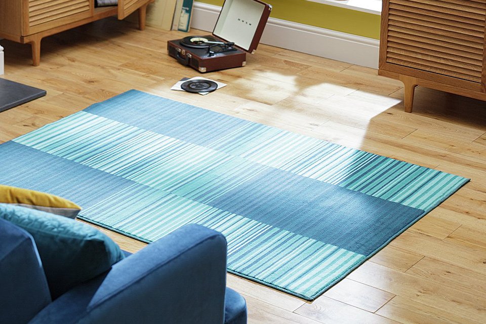 Image of striped blue rug on wooden floor next to blue armchair.