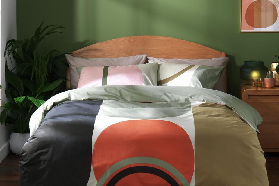 A wooden bed with geo print bedding in pink, orange, black and green. 