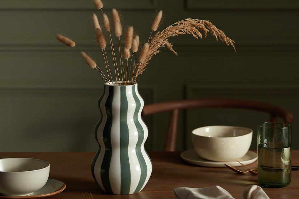 Habitat Hand Painted Stripe Vase in green colour placed on a wooden dining table.